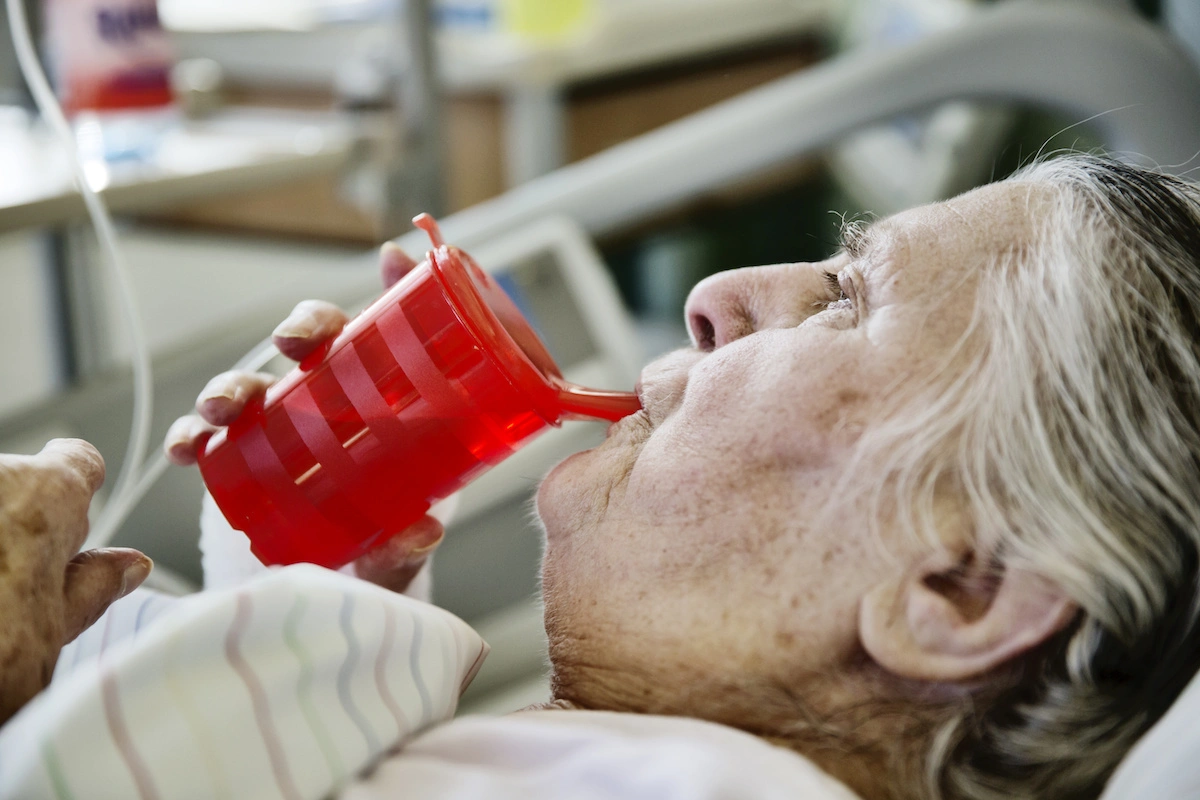 Seniorin im Krankenhaus trinkt aus einer Schnabeltasse