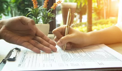 The human hand with pen is signing on The Insurance Claim Form,on wooden desk,vintage tone.