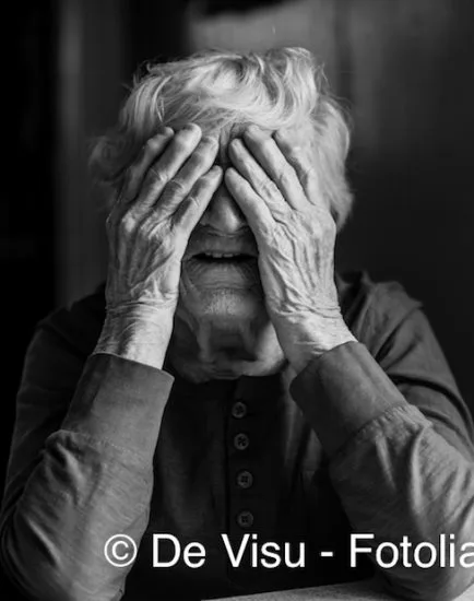 An elderly woman covers her face with wrinkled hands. Black and white photo.