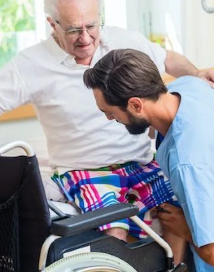 Elderly care nurse in retirement home helping senior from wheel chair to bed