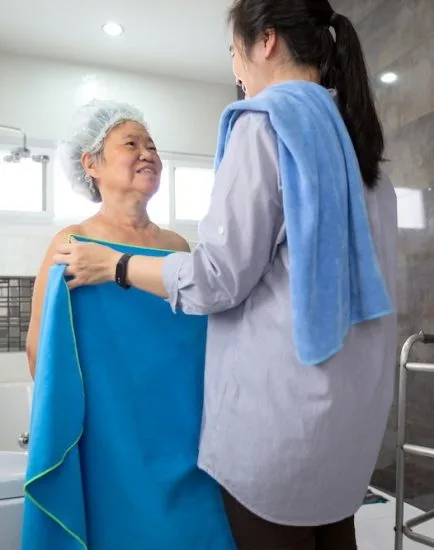 Asian daughter or female care assistant help her senior mother wipe her body after shower in bathroom at home,service,support,safety of elderly people and family relationships concept
