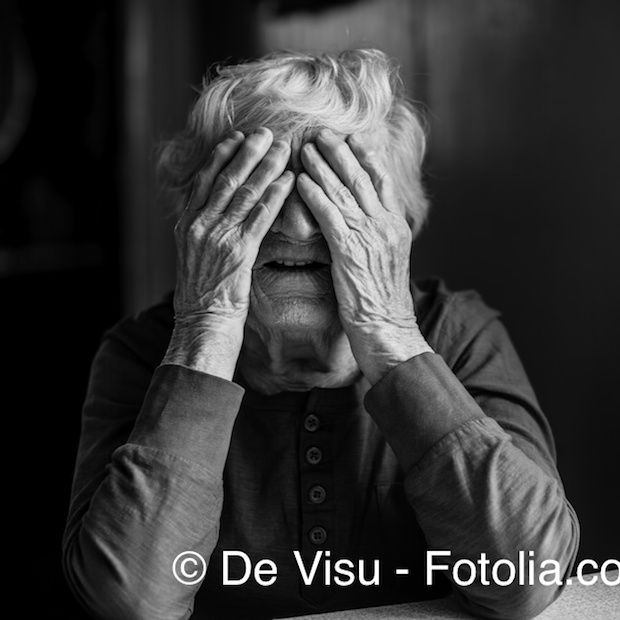 An elderly woman covers her face with wrinkled hands. Black and white photo.