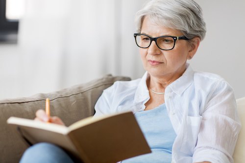 senior woman writing to notebook or diary at home