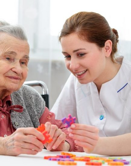 Elder care nurse playing jigsaw puzzle with senior woman in nursing home