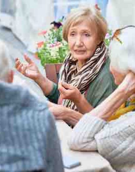 Portrait of senior people enjoying dinner together, focus on lady telling stories to friends gesturing actively