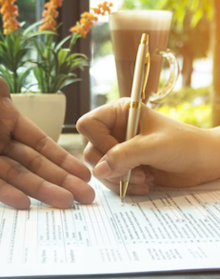 The human hand with pen is signing on The Insurance Claim Form,on wooden desk,vintage tone.