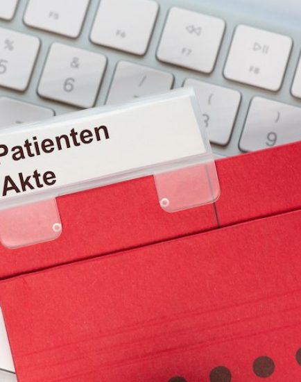 Roter Hängehefter mit Reiter und dem Text: Patienten Akte. Der Ordner liegt auf einem Computer Keyboard,