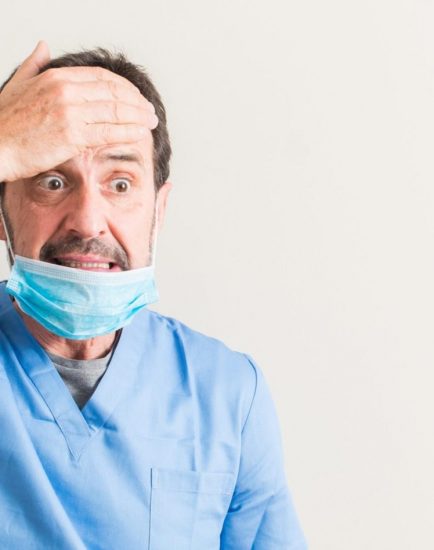 Senior doctor man using mask stressed with hand on head, shocked with shame and surprise face, angry and frustrated. Fear and upset for mistake.