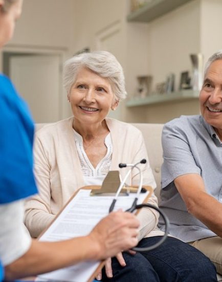 Nurse during home visit with senior couple. Doctor holding clipboard and stethoscope in conversation with old couple at home. Nurse bringing home the results of medical exams.