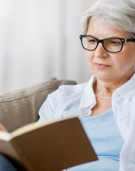 age, leisure and people concept - close up of senior woman in glasses writing to notebook or diary at home